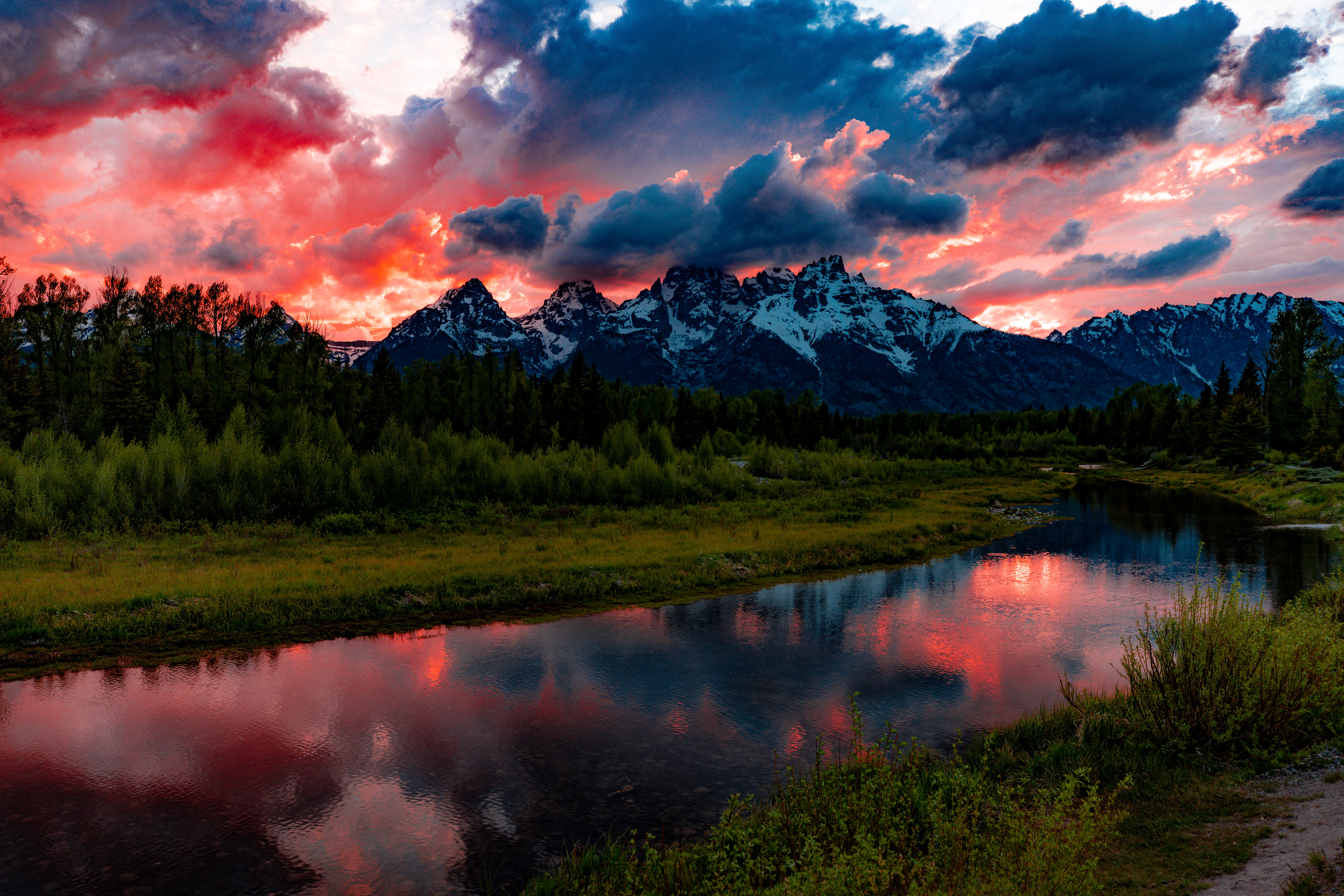 Sunset casting a golden glow over the Tetons, with rugged peaks silhouetted against an orange and pink sky.
