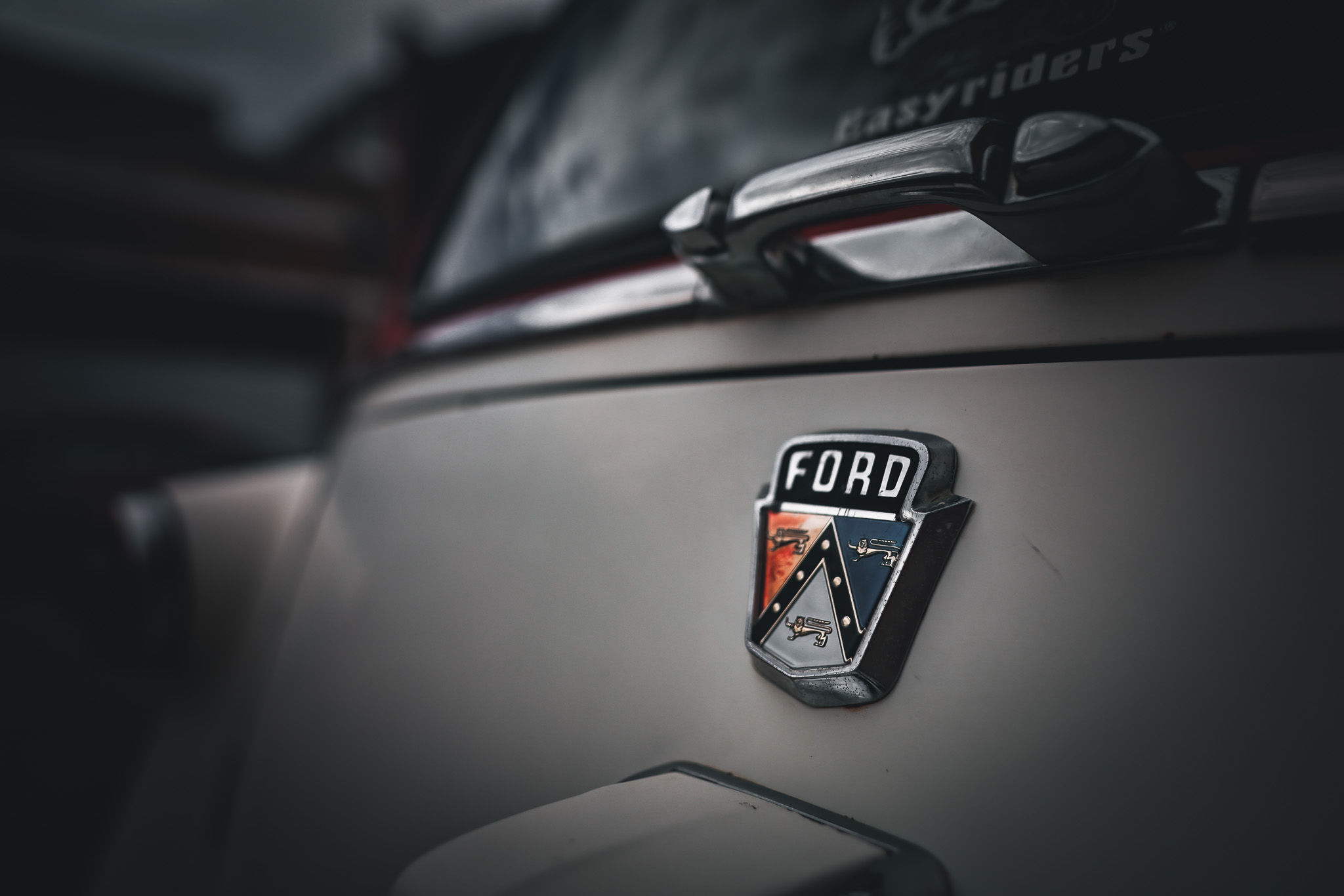 Close-up of an old Ford logo on a classic car, with the emblem's intricate details and vintage styling clearly visible.