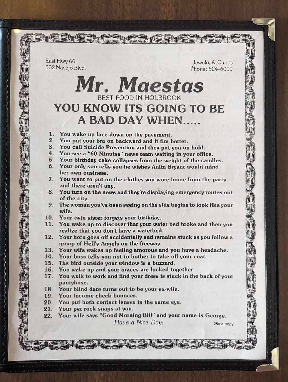 Humorous list titled "You Know It's Going To Be A Bad Day When..." on restaurant menu, with funny scenarios in a bordered frame on a wooden surface.
