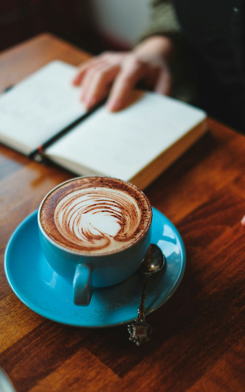 Tazza con cappuccino e mano su un quaderno aperto sullo sfondo