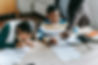 Two young students doing schoolwork at their desk while the teacher helps