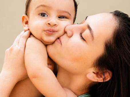 Mère embrassant son bébé dans les bras, fond beige, moment tendre et doux.