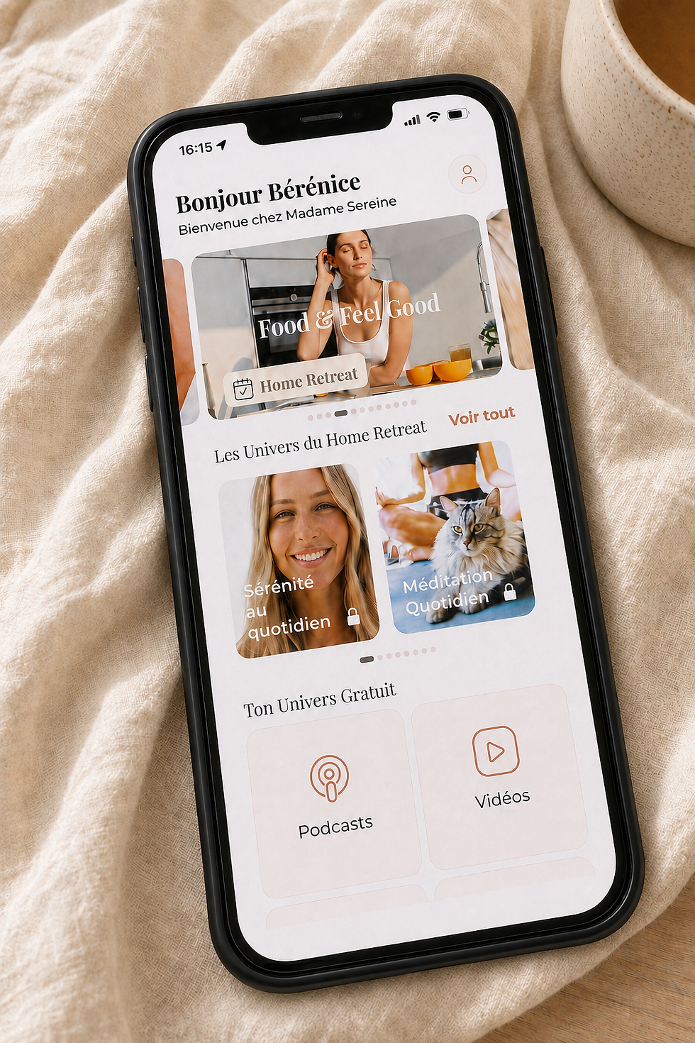 Écran d’un iPhone sur tissu beige affichant une appli bien-être: Bonjour Bérénice, Home Retreat, Podcasts et Vidéos.