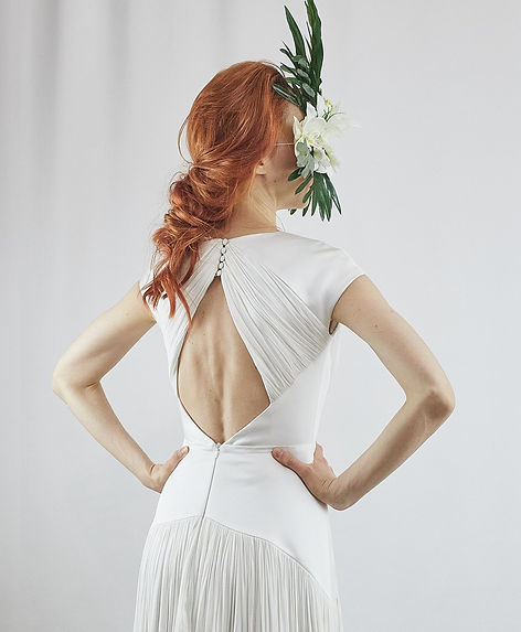 Modelo peliroja de espaldas con un tocado de flores y vestido de novia sencillo