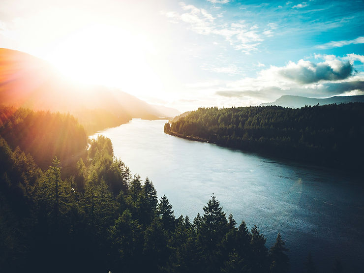 Sunset over a serene river, surrounded by dense green forests. The sky is blue with scattered clouds, creating a tranquil and peaceful atmosphere. Water law in Washington state.