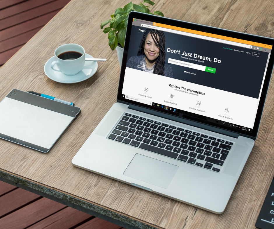 A laptop on the table beside a notebook, displaying the website Fiverr in the web browser.