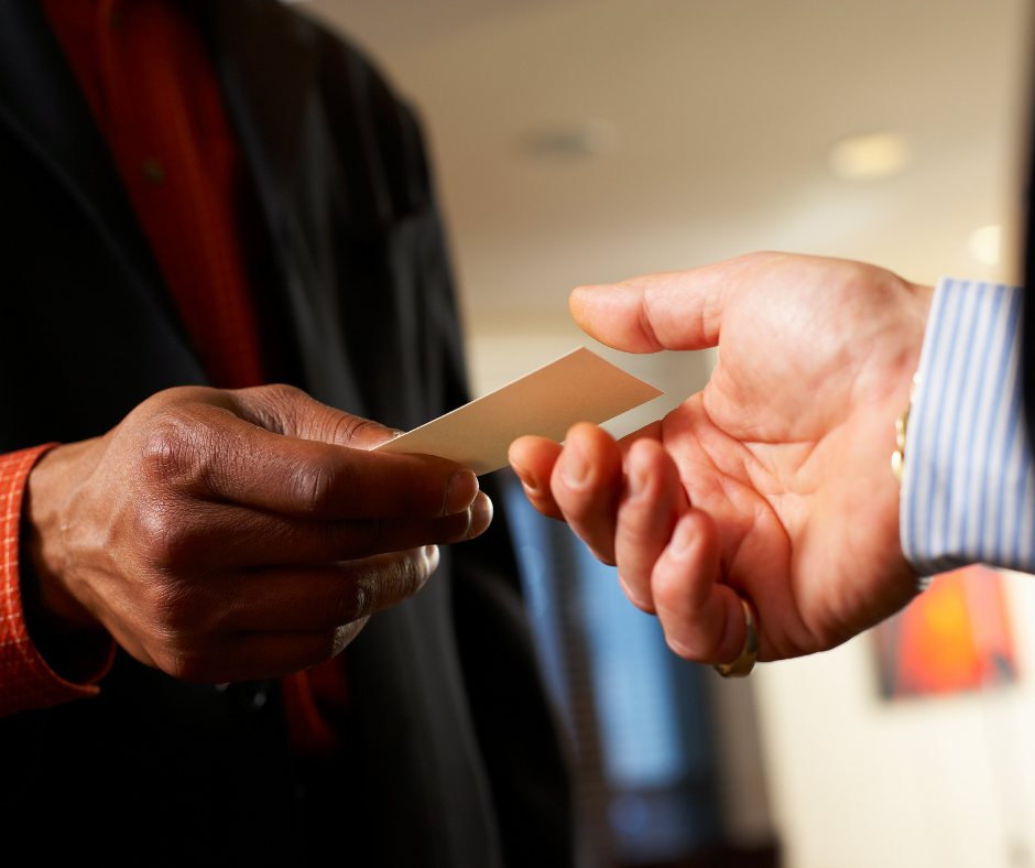 A man handing out his business card to another at a networking event.