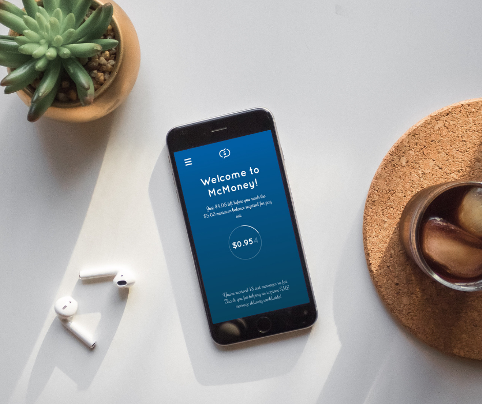 A phone on a desk besides a cup, showing the McMoney app.