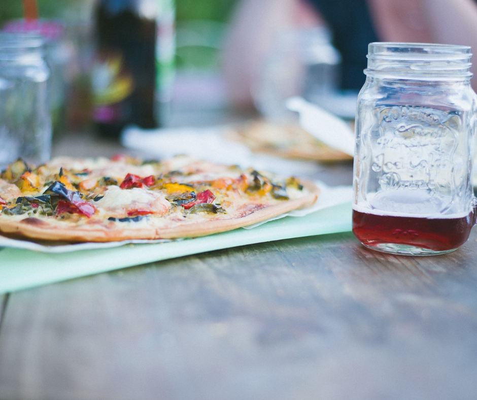 A pizza besides a mason jar containing juice on a table at a restaurant.