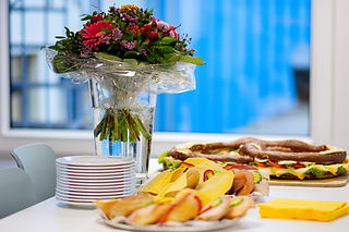 Ein Tisch mit einem Blumenstrauß und belegten Brötchen.
