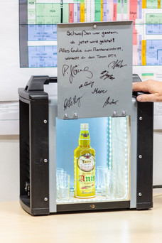 Eine Box mit Schnaps drin und einem Blech mit Unterschriften drauf.