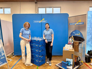 Zwei Kolleginnen vor einer blauen Messewand auf einer Messe