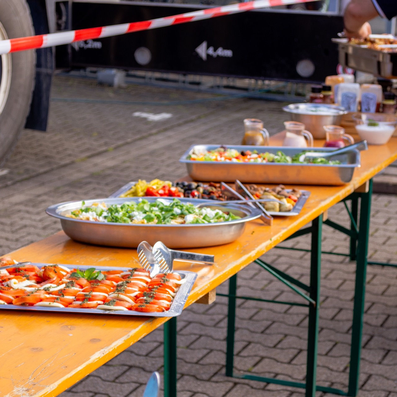 Eine lange Tischreihe. Auf den Tischen steht essen.