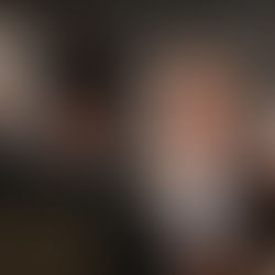 Mann im Anzug lächelt in die Kamera. Im Vordergrund haben zwei Männer dem Fotografen den Rückenzugewandt.