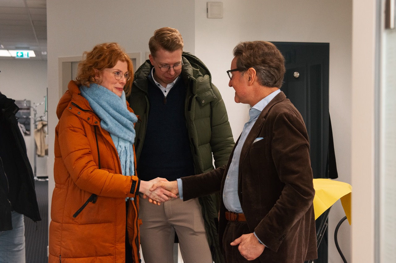 Zwei Personen schütteln sich die Hand. Eine dritte Person schaut zu.