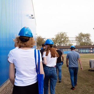 Mehrere Personen die an einer Halle entlanglaufen und Helme tragen.