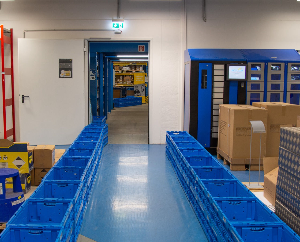 Ein Raum wo links und rechts Box aufgestellt sind. Die Boxen bilden einen Weg hin zu einer Tür.