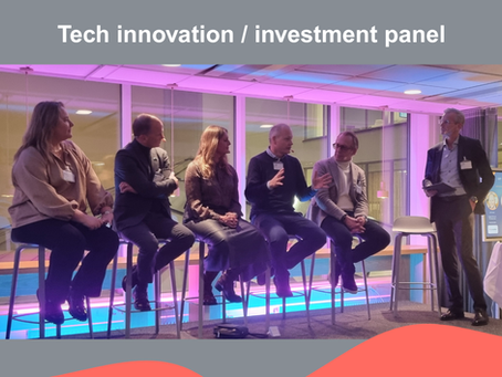 Five people (two women and three men) sitting on bar stools on a stage. One man in a suit standing to the right, holding some notes in his hand. Heading above saying "Tech innovation / investment panel". Red wave pattern at the bottom.