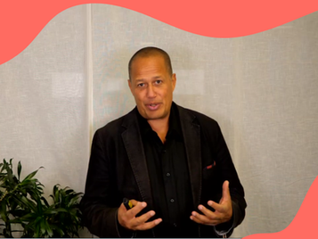Close-up of man in black next to a plant in an office. Red wave pattern at the top and bottom right.