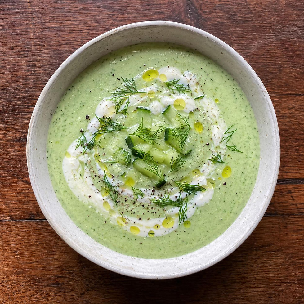 Grüne Suppe in weißer Schüssel auf Holztisch. Mit saurer Sahne, Gurkenstücken, Dill und Öltropfen garniert. Frischer, sommerlicher Look.