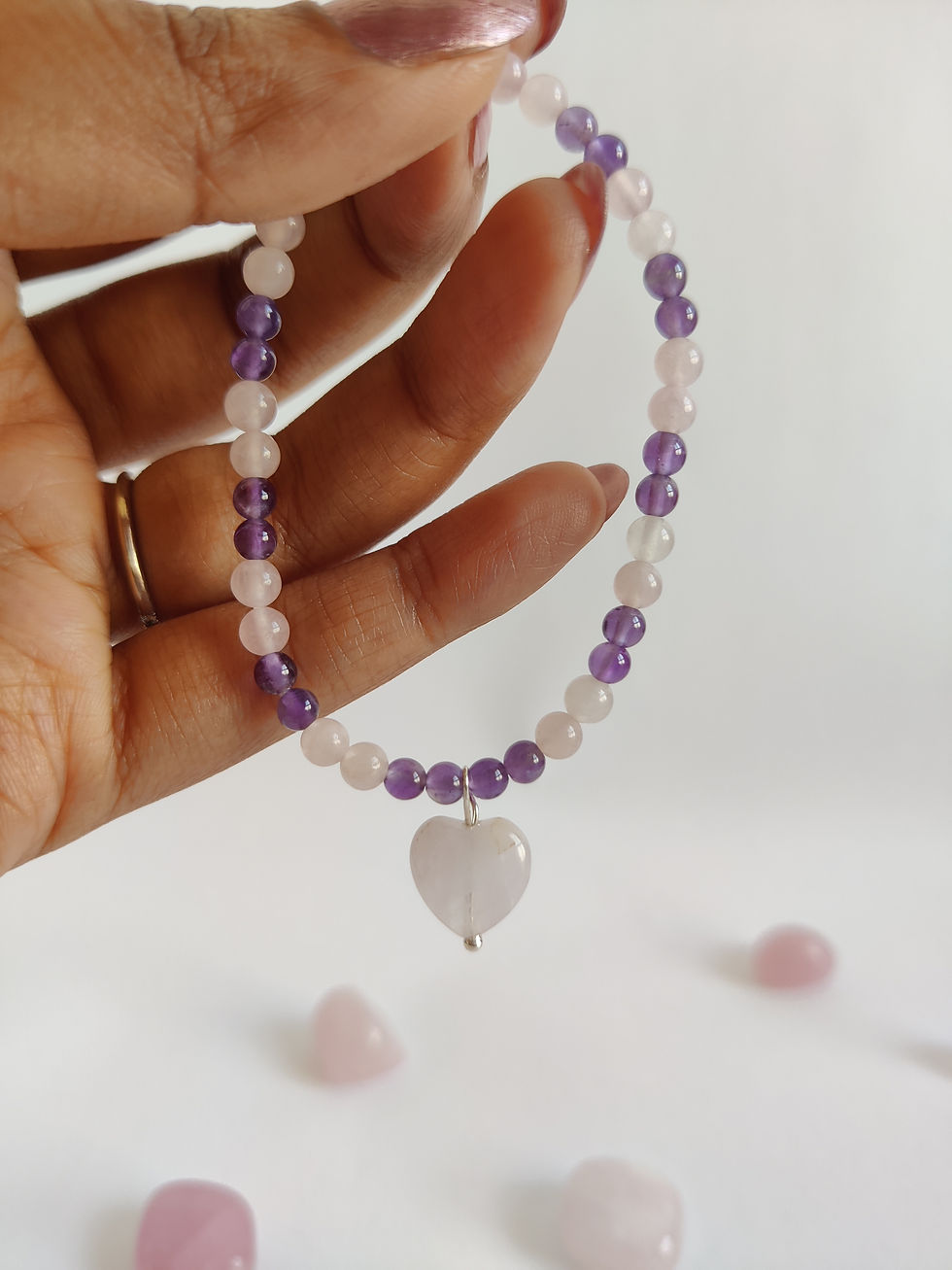Close-up of a delicate pink Rose Quartz bead bracelet with purple Amethyst accent stones and a small heart charm.