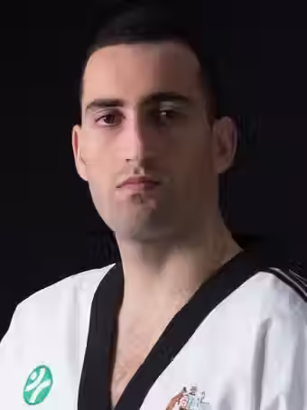 Arash Mozhdeh, head instructor at Mozhdeh Martial Arts, wearing a white Taekwondo uniform with black collar, facing forward against a dark background