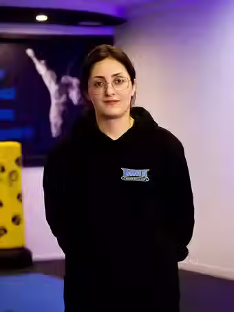 Behnaz Mozhdeh, head coach at Mozhdeh Martial Arts, wearing a black MMA hoodie, standing in the gym with a calm expression
