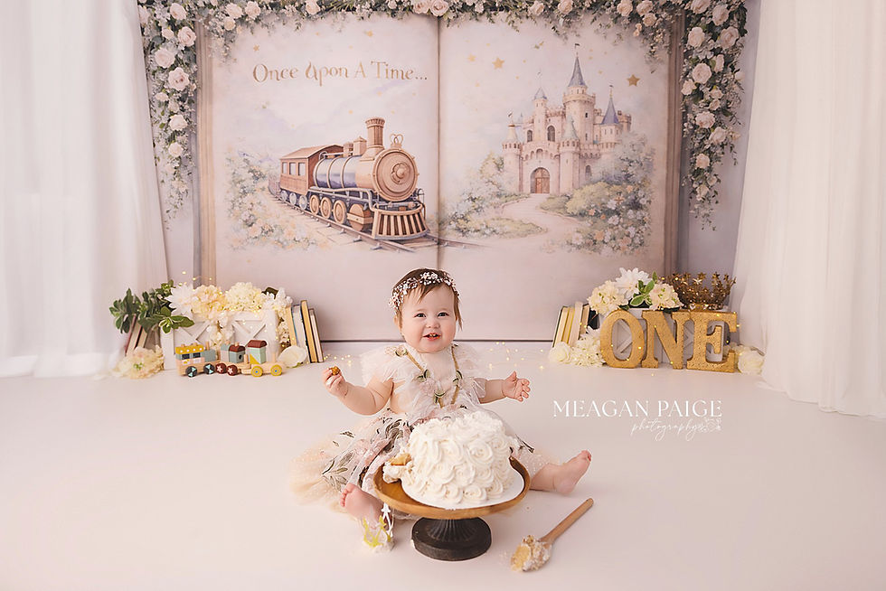 Smiling baby in floral dress sits with cake. "Once Upon a Time" backdrop with train and castle, surrounded by flowers and toys. "ONE" sign.