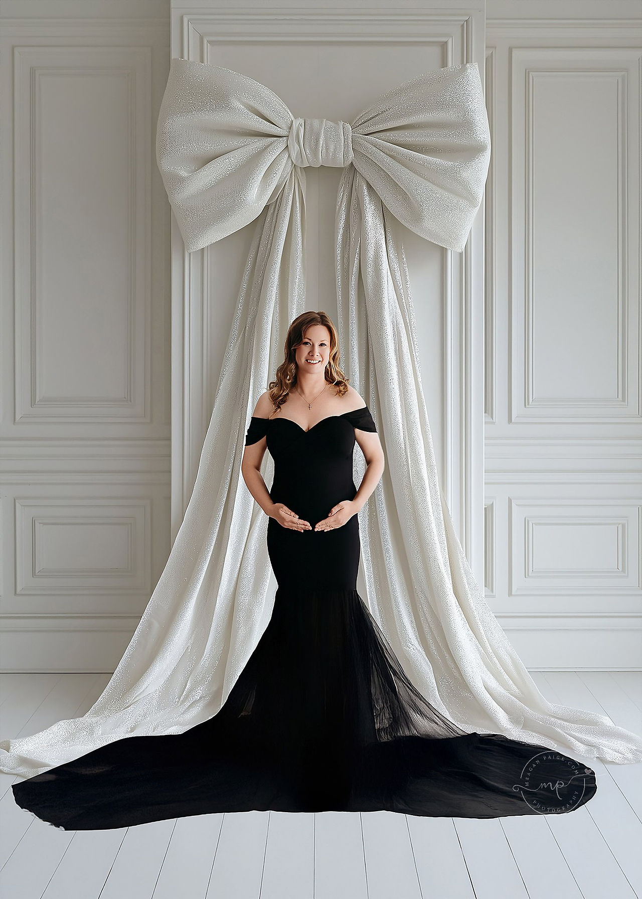 Elegant maternity portrait of a woman in a champagne gown sitting on a white bench with a golden backdrop at a Calgary luxury maternity photography studio.