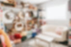 Cozy Newborn Prop Room room with white couch and pink pillow, shelves of baskets, moon shapes, and colorful fabrics. Bright window adds warmth.