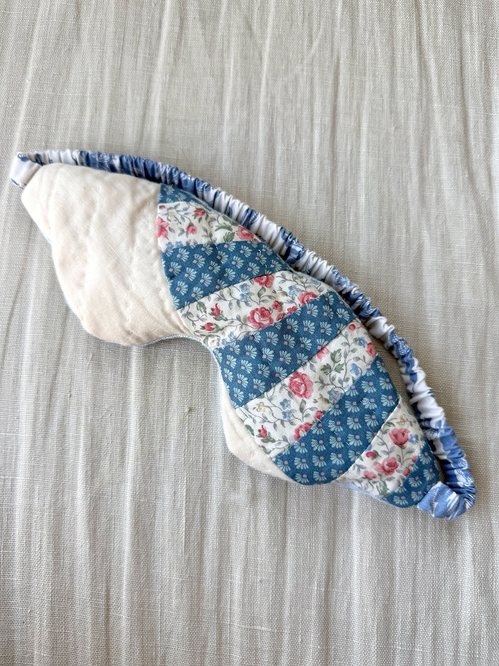 Cushioned handmade eye mask made from a vintage patchwork quilt showing detailed blue floral patterns and cream accents.