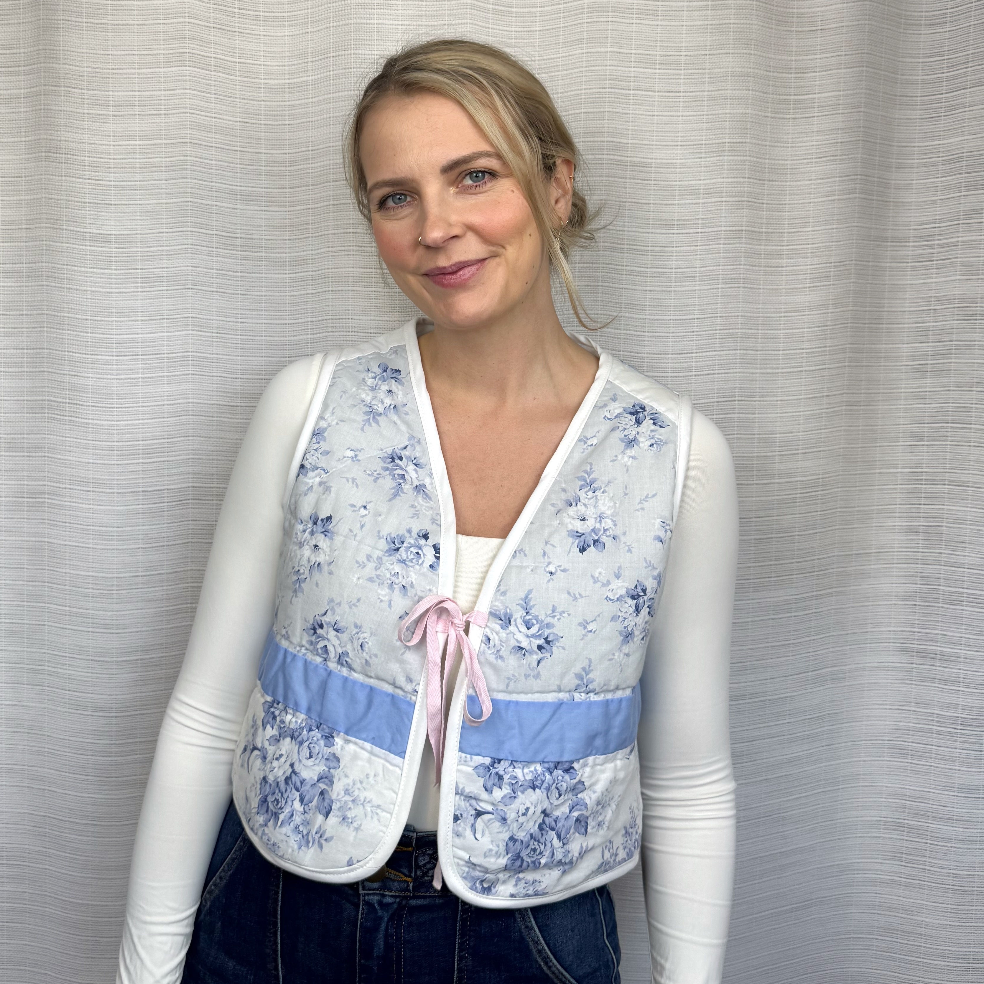 Upcycled blue floral quilted vest with pink ribbon tie, front view on model.