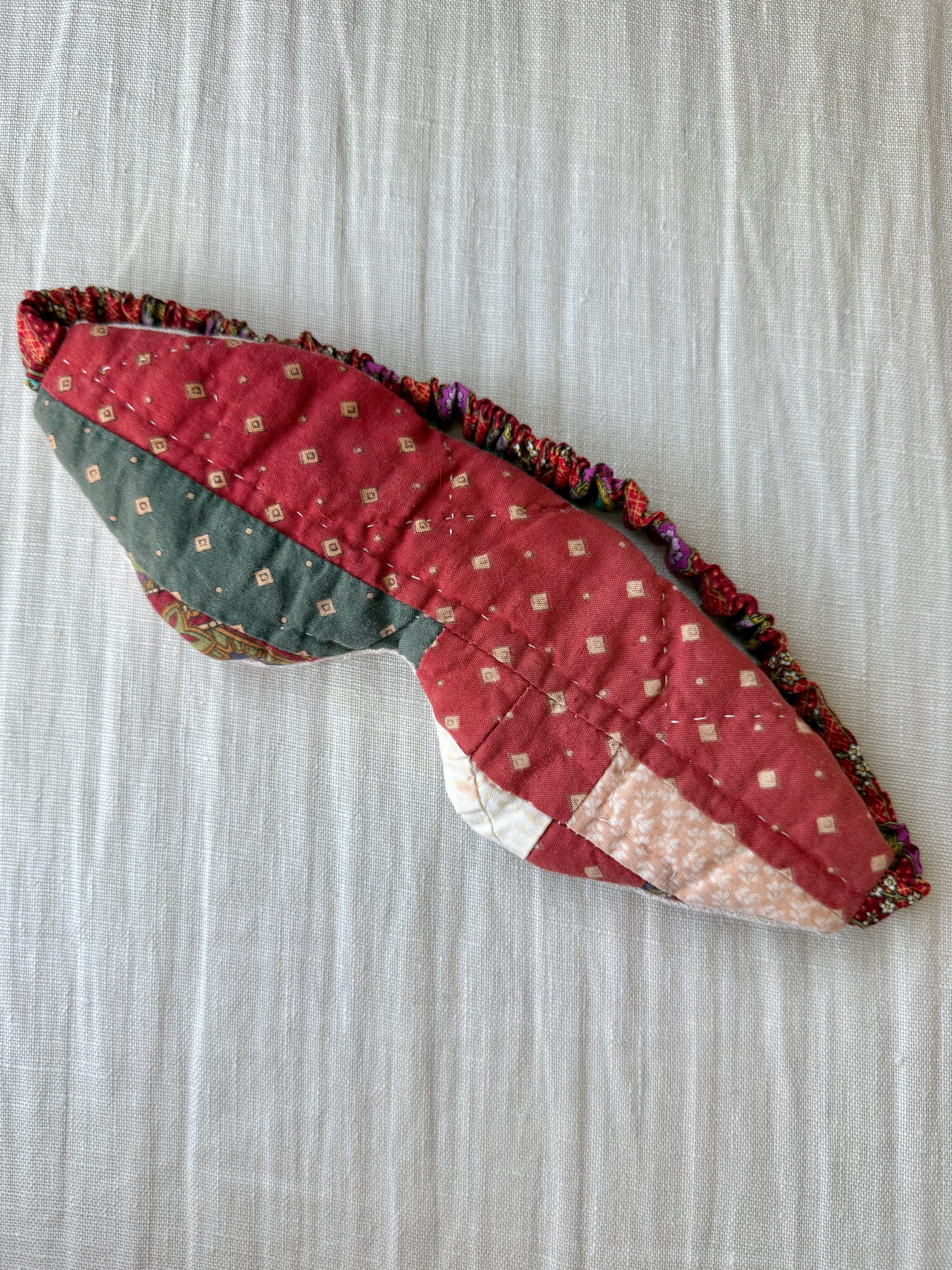 Upcycled vintage quilt eye mask for meditation featuring a rustic rust red and deep green patchwork design.