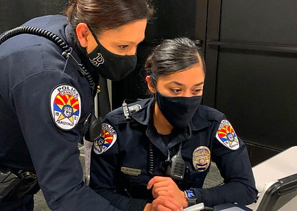 Female police officers with masks on viewing a computer screen.