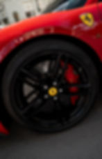 Černé kolo vozu Ferrari s červeným brzdovým třmenem.