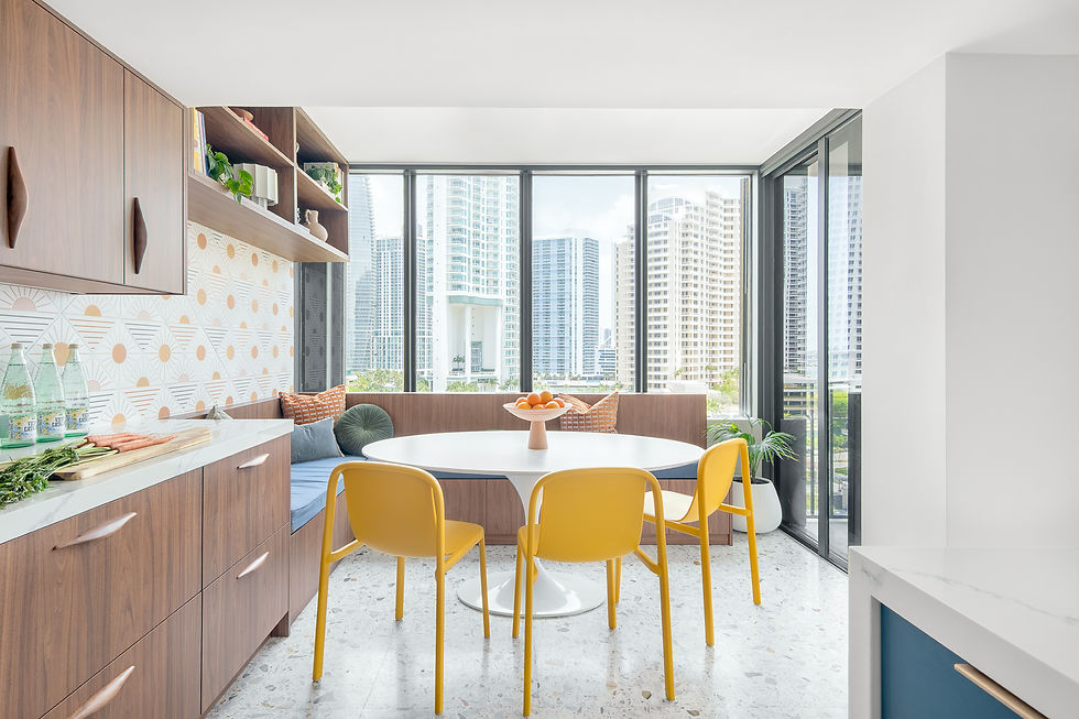 Bright modern dining nook with yellow chairs, round white table, fruit bowl, and city skyline through large windows.