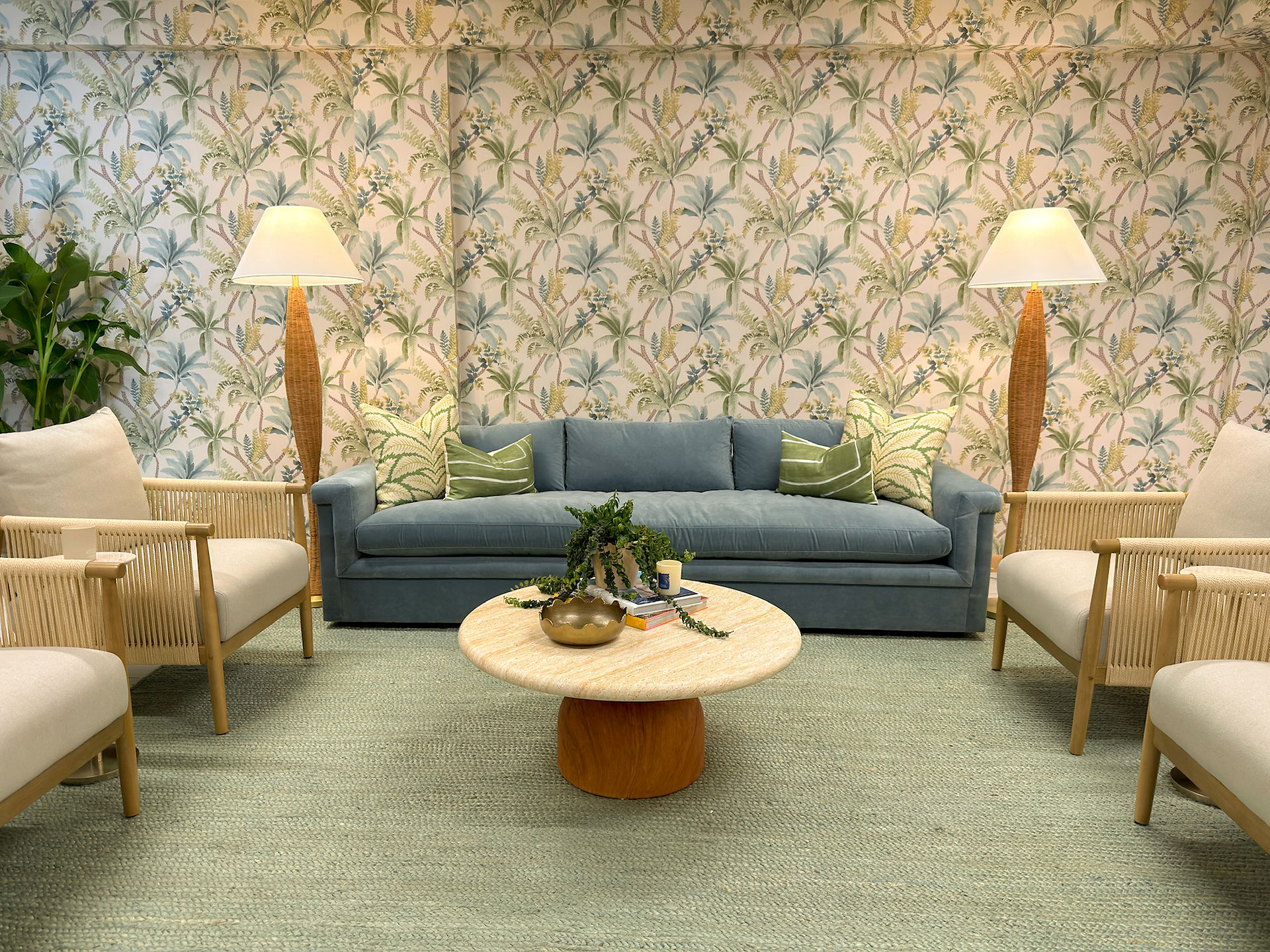 Cozy tropical lounge with rattan chairs, green pillows, framed beach photos, and leafy wallpaper in a bright, calm setting