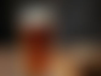 Gros plan sur un verre de bière Amber Lager de la Brasserie de la Sainte-Baume, révélant une robe cuivrée limpide et une mousse crémeuse, posé sur une table en bois rustique à côté d'une miche de pain de campagne.