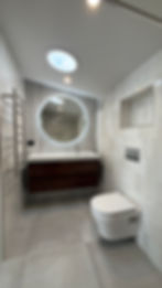 Bathroom shower with full-height wall tiling and round backlit mirror above the vanity