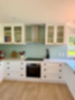 White shaker-style kitchen with pale blue subway tile backsplash, glass-front cabinets, and black cooktop