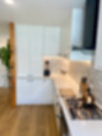 Renovated kitchen with white cabinetry, tall pantry, black rangehood and gas cooktop