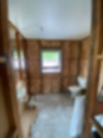 Small bathroom mid-renovation with insulation exposed in the walls and toilet on the floor