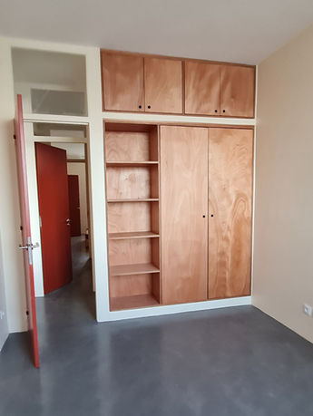 Aménagement dressing sur mesure avec étagères ouvertes et placards en bois, porte rouge foncé en arrière-plan – rénovation appartement années 50