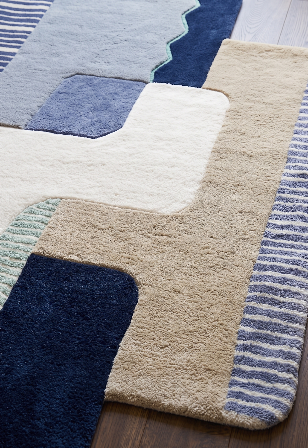 Overhead view of a hand tufted abstract geometric wool rug featuring blue striped panels and tan color blocks on a wood floor