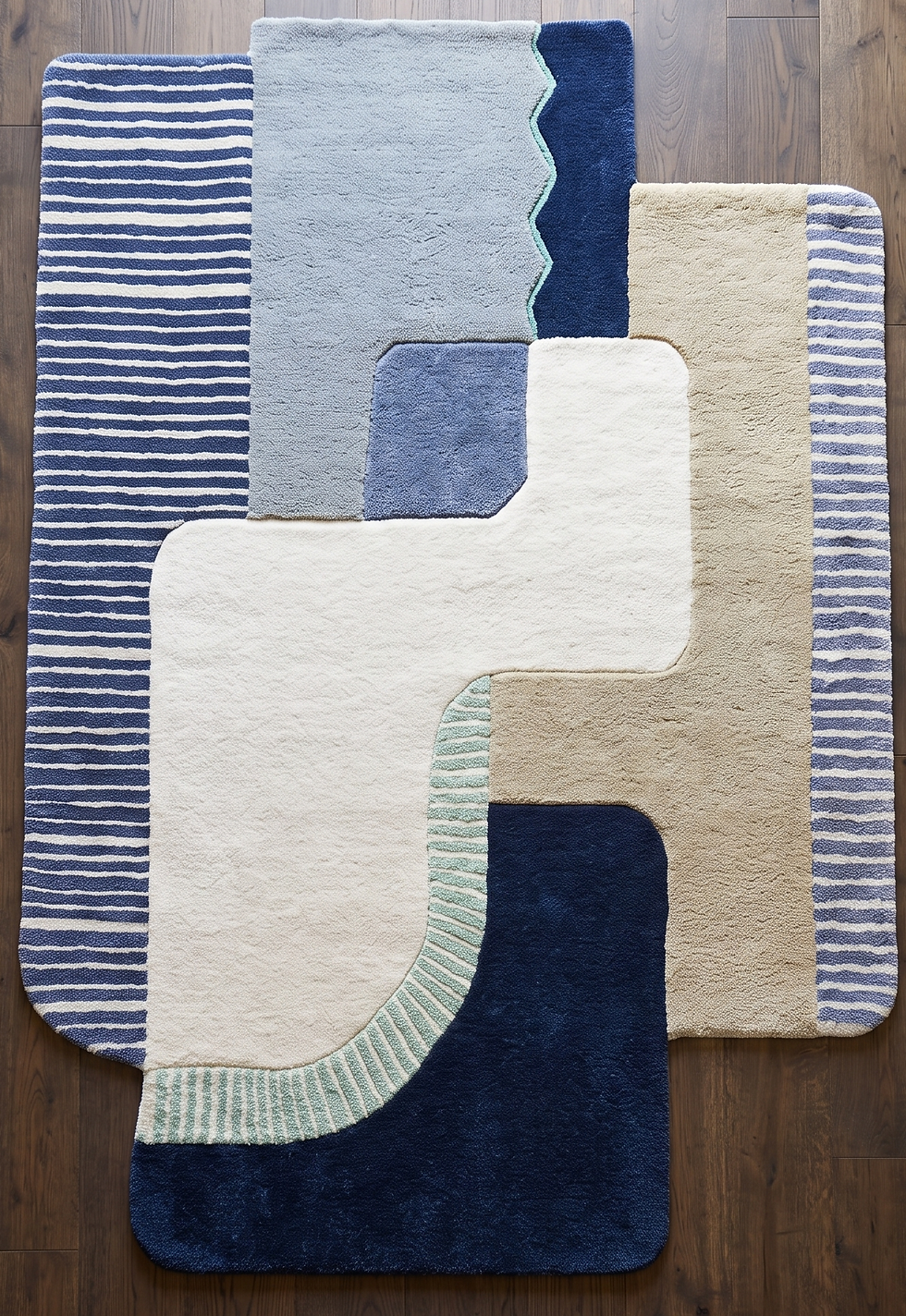 Overhead view of a hand tufted abstract geometric wool rug featuring blue striped panels and tan color blocks on a wood floor