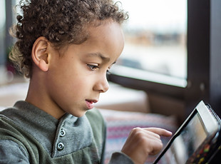 A young boy with medium-dark skin tone plays on tablet