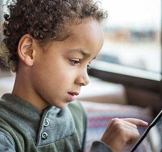 Young curly, brown haired boy playing on a tablet