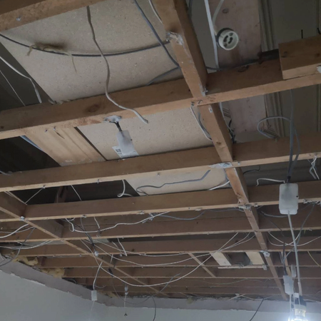 Ceiling stripped back revealing old wiring, pipework, and historic decorative plaster hidden above