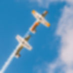 Two small planes preforming a stunt together rising up into the sky.
