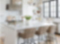 A crisp, white and clean kitchen with chairs around a centre island.